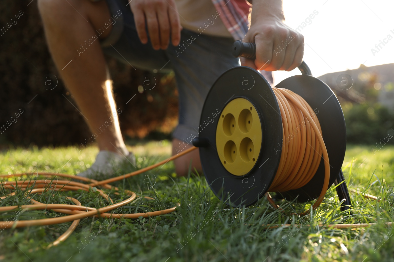 Photo of Man with extension cord reel on green grass outdoors, closeup