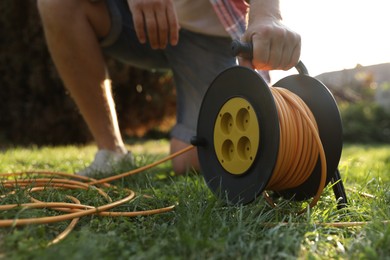 Man with extension cord reel on green grass outdoors, closeup