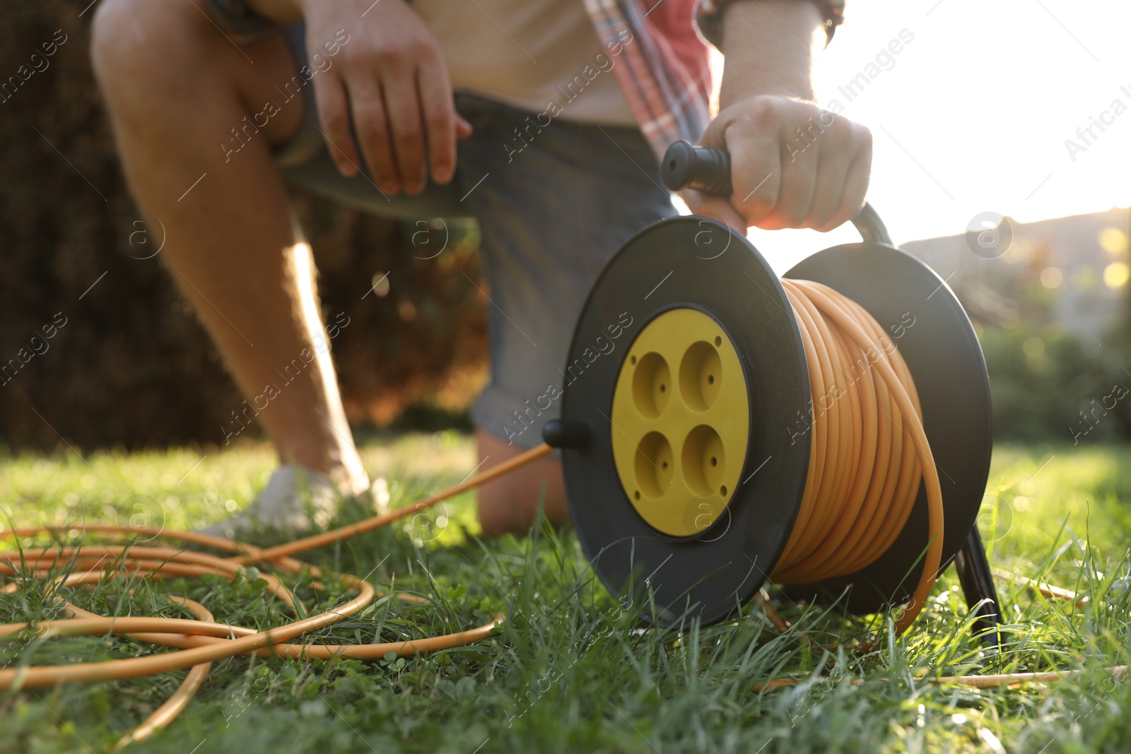 Photo of Man with extension cord reel on green grass outdoors, closeup