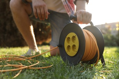 Man with extension cord reel on green grass outdoors, closeup