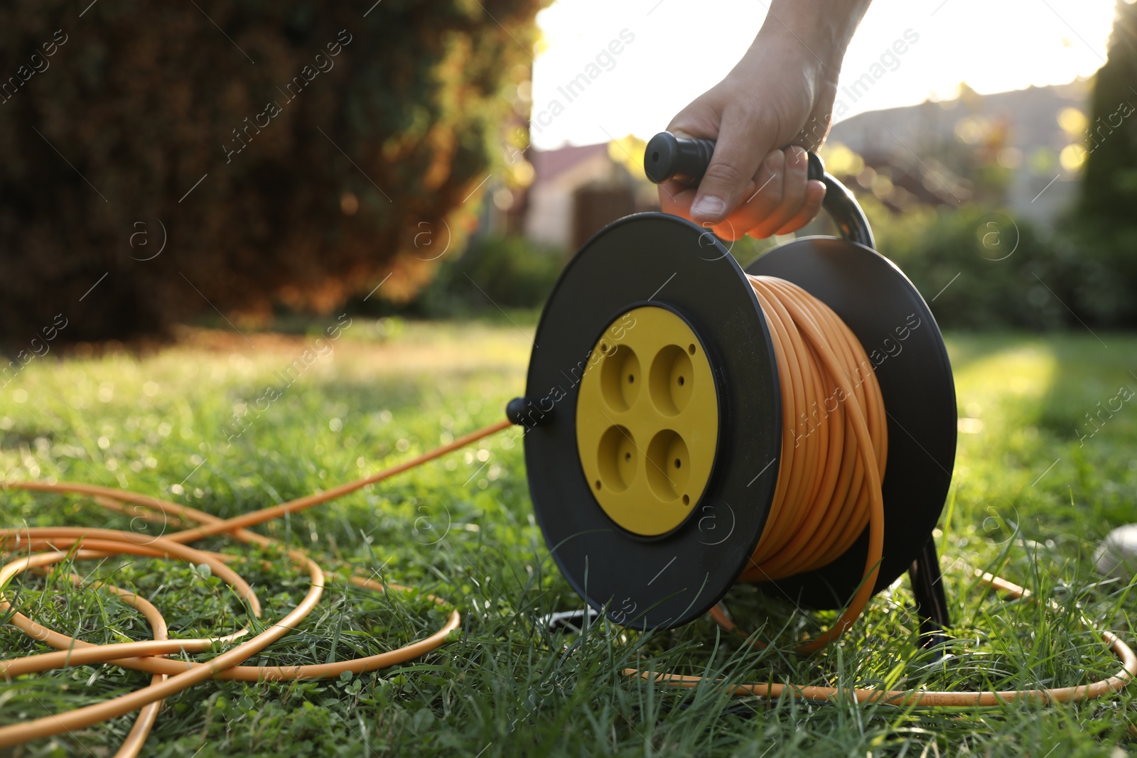 Photo of Man with extension cord reel on green grass outdoors, closeup