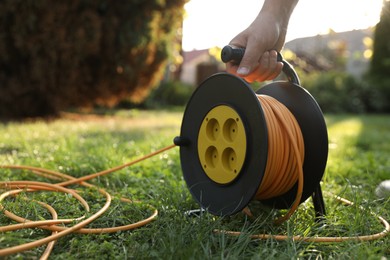 Photo of Man with extension cord reel on green grass outdoors, closeup