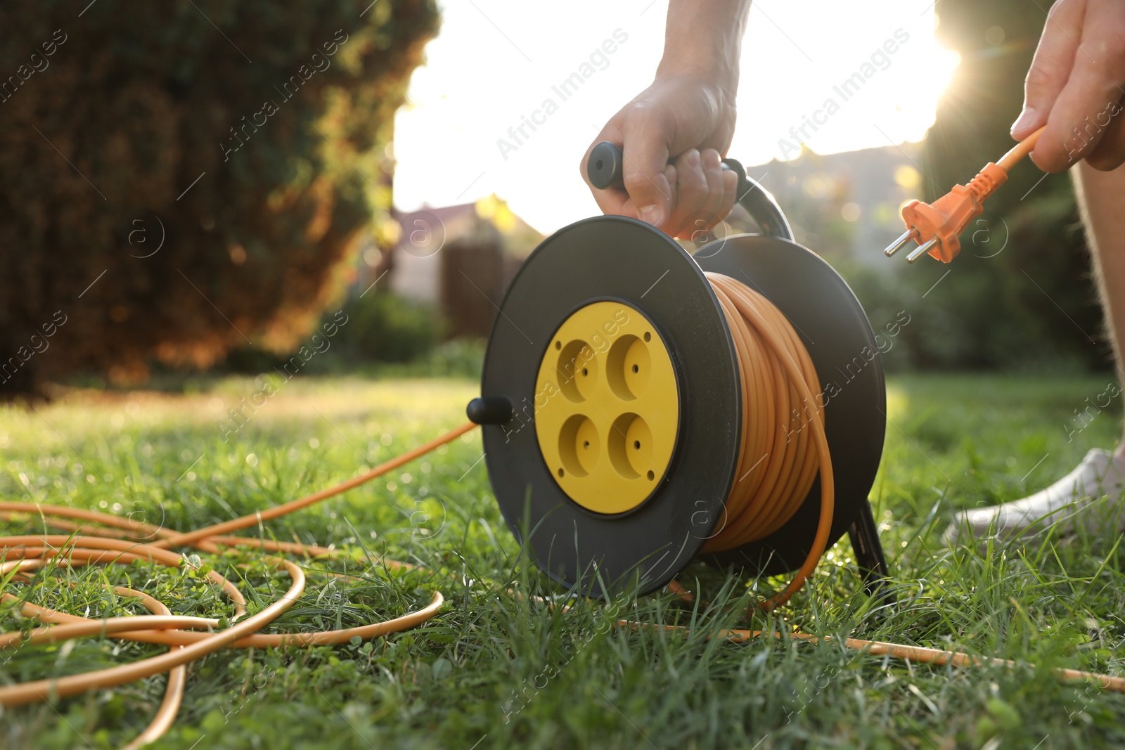 Photo of Man with extension cord reel on green grass outdoors, closeup