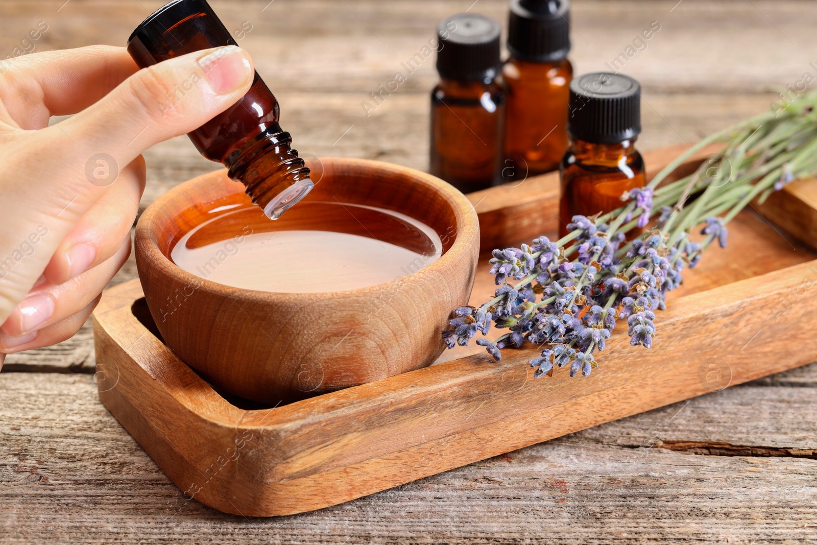 Photo of Woman dripping essential oil into bowl with water at wooden table, closeup