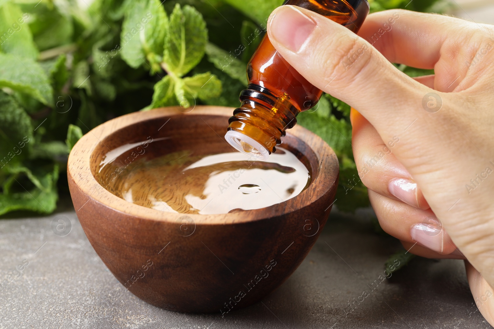 Photo of Woman dripping essential oil into bowl with water at grey table, closeup