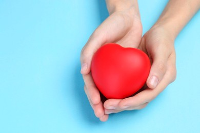 Photo of Woman holding red heart on light blue background, closeup. Space for text