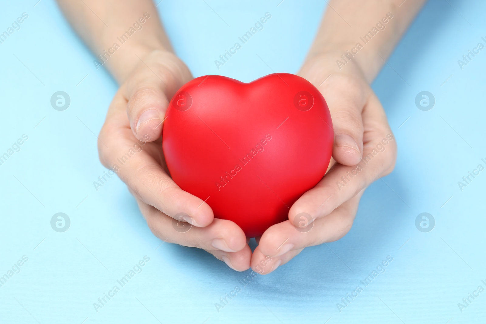 Photo of Woman holding red heart on light blue background, closeup