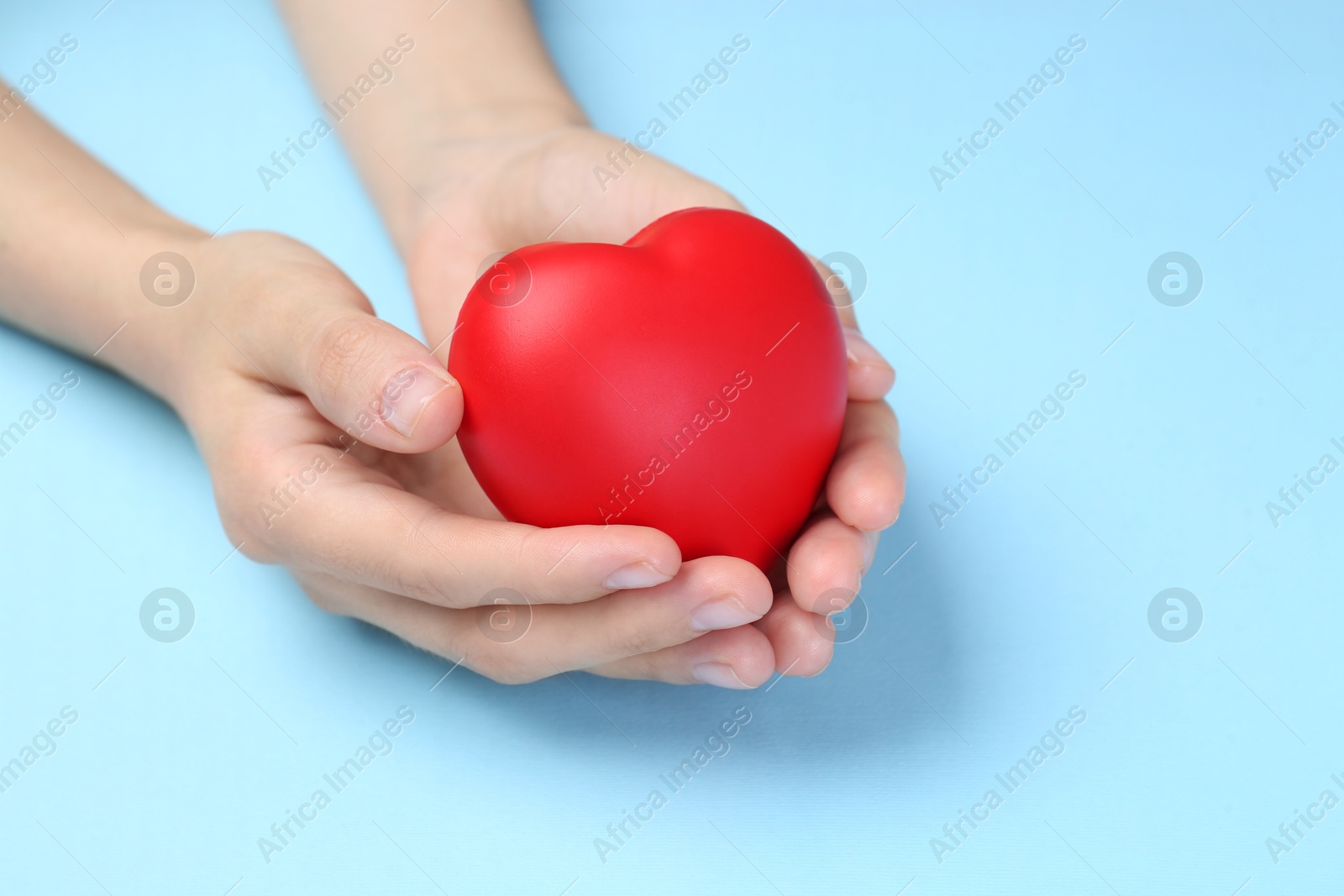 Photo of Woman holding red heart on light blue background, closeup