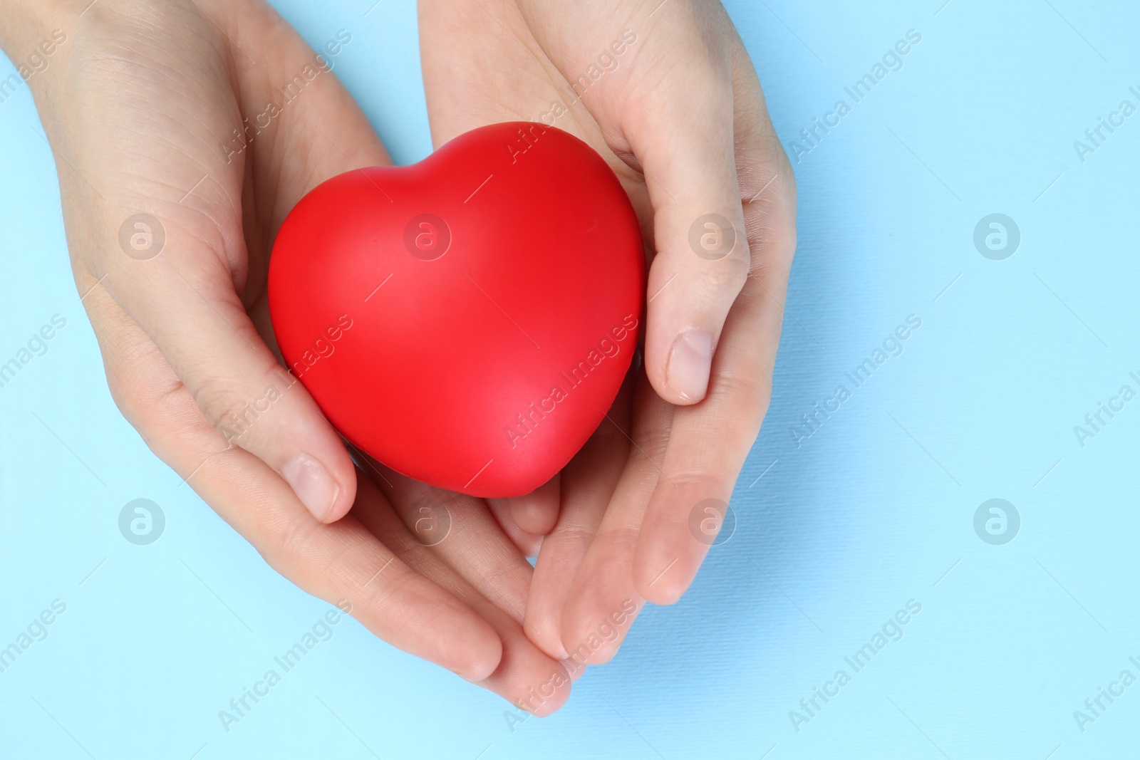 Photo of Woman holding red heart on light blue background, top view