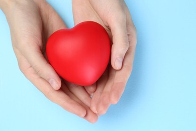 Woman holding red heart on light blue background, top view