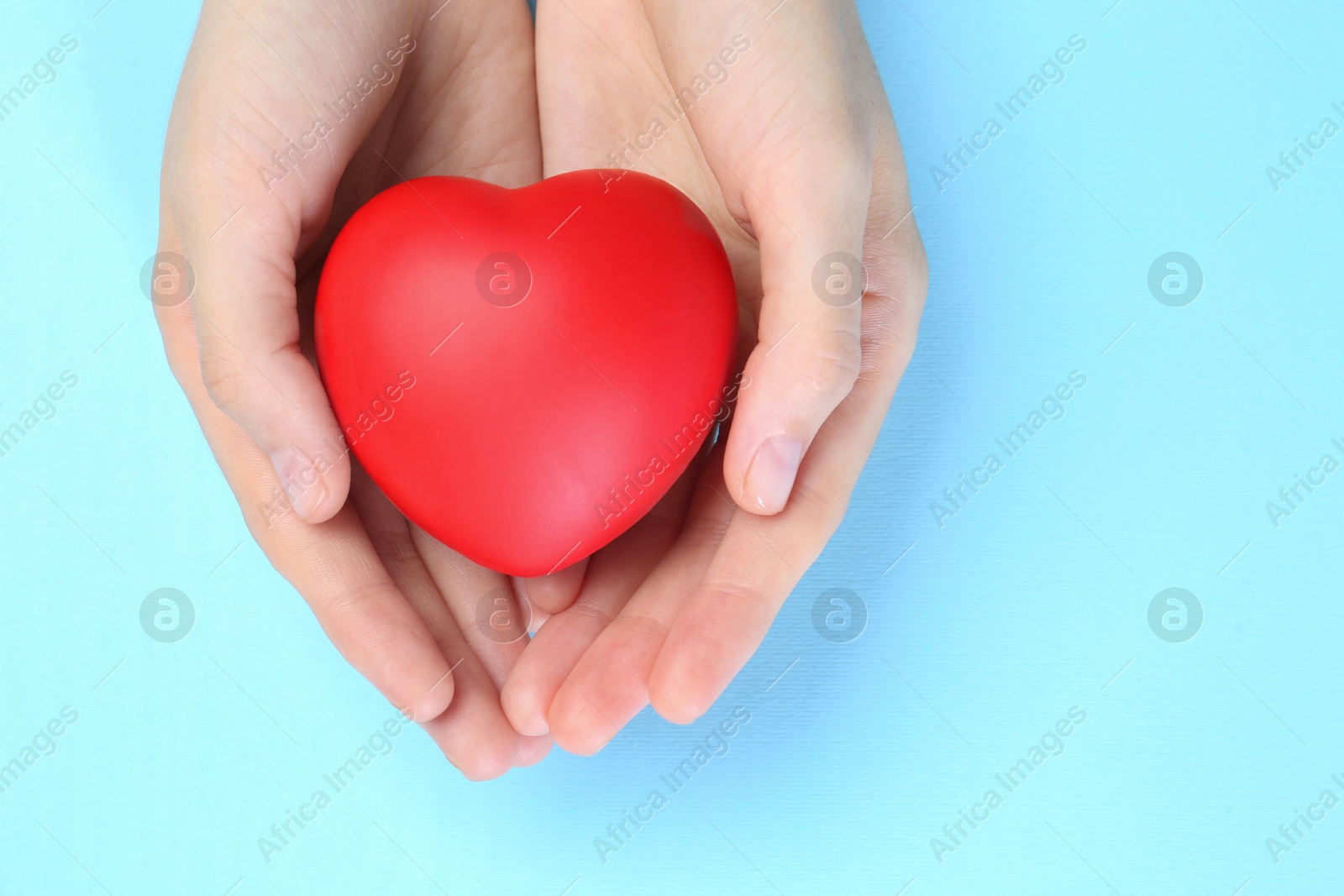 Photo of Woman holding red heart on light blue background, top view