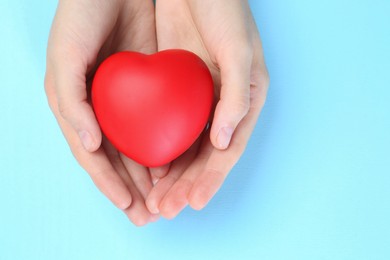 Photo of Woman holding red heart on light blue background, top view