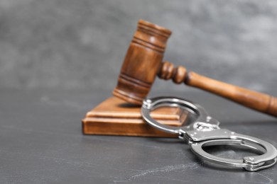 Photo of Judge's gavel and handcuffs on gray textured table, closeup. Space for text