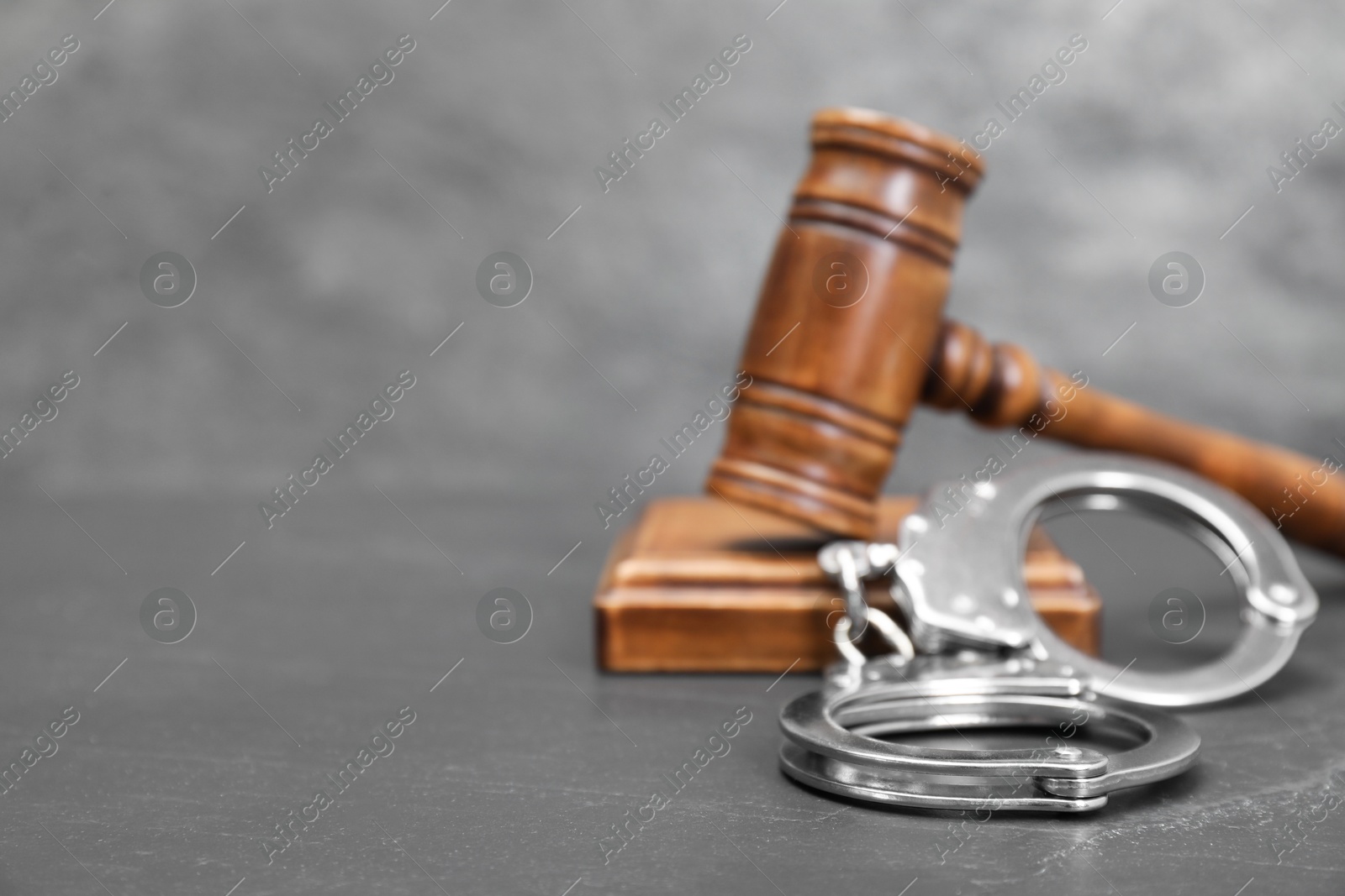 Photo of Judge's gavel and handcuffs on gray textured table, closeup. Space for text