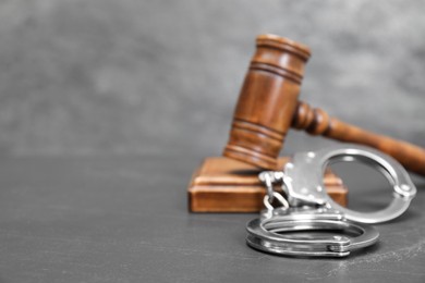 Photo of Judge's gavel and handcuffs on gray textured table, closeup. Space for text