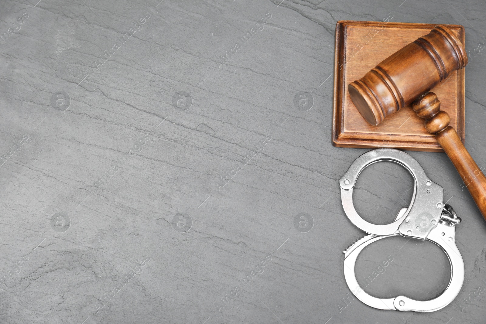 Photo of Judge's gavel and handcuffs on gray textured table, flat lay. Space for text