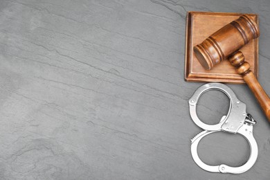 Photo of Judge's gavel and handcuffs on gray textured table, flat lay. Space for text