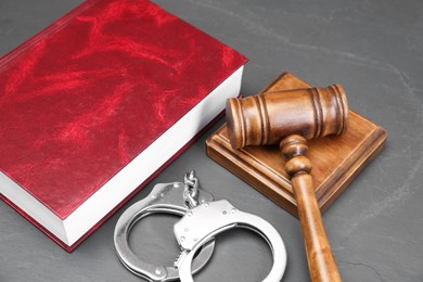 Book, judge's gavel and handcuffs on gray textured table