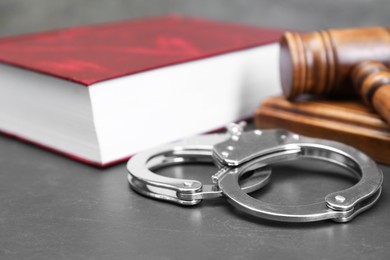 Photo of Book, judge's gavel and handcuffs on gray textured table, closeup