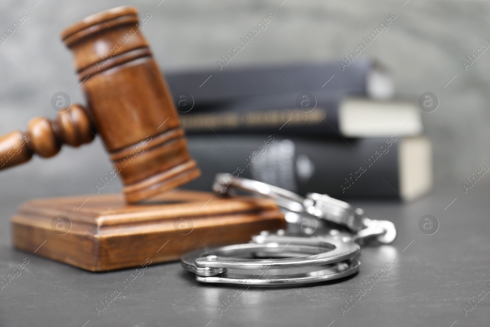 Photo of Books, judge's gavel and handcuffs on gray textured table, selective focus