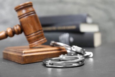 Photo of Books, judge's gavel and handcuffs on gray textured table, selective focus