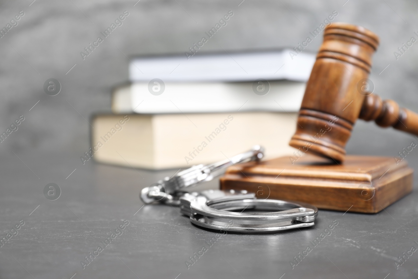 Photo of Books, judge's gavel and handcuffs on gray textured table, selective focus