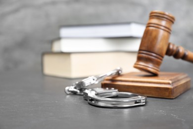 Photo of Books, judge's gavel and handcuffs on gray textured table, selective focus