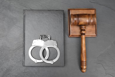 Book, judge's gavel and handcuffs on gray textured table, flat lay