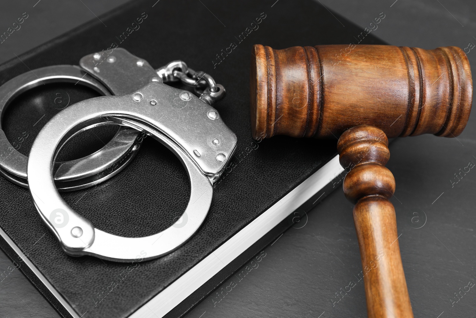 Photo of Book, judge's gavel and handcuffs on gray textured table, closeup