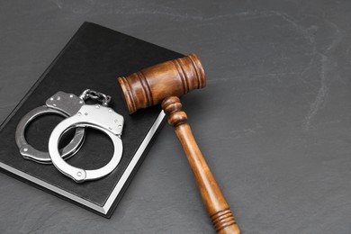 Book, judge's gavel and handcuffs on gray textured table, space for text