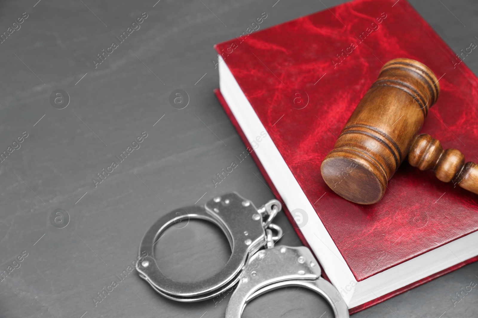 Photo of Book, judge's gavel and handcuffs on gray textured table, space for text