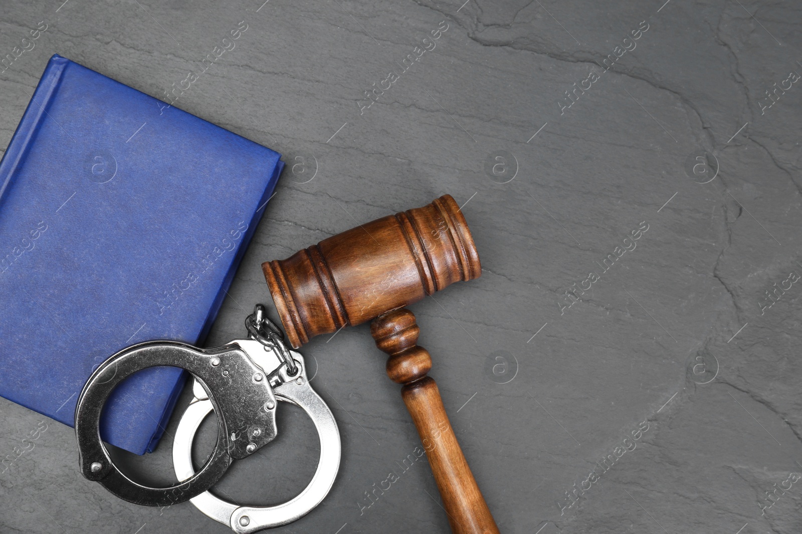 Photo of Book, judge's gavel and handcuffs on gray textured table, flat lay. Space for text