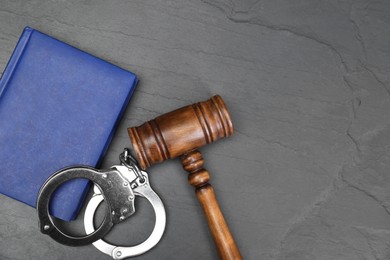 Book, judge's gavel and handcuffs on gray textured table, flat lay. Space for text