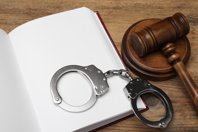 Book, judge's gavel and handcuffs on wooden table