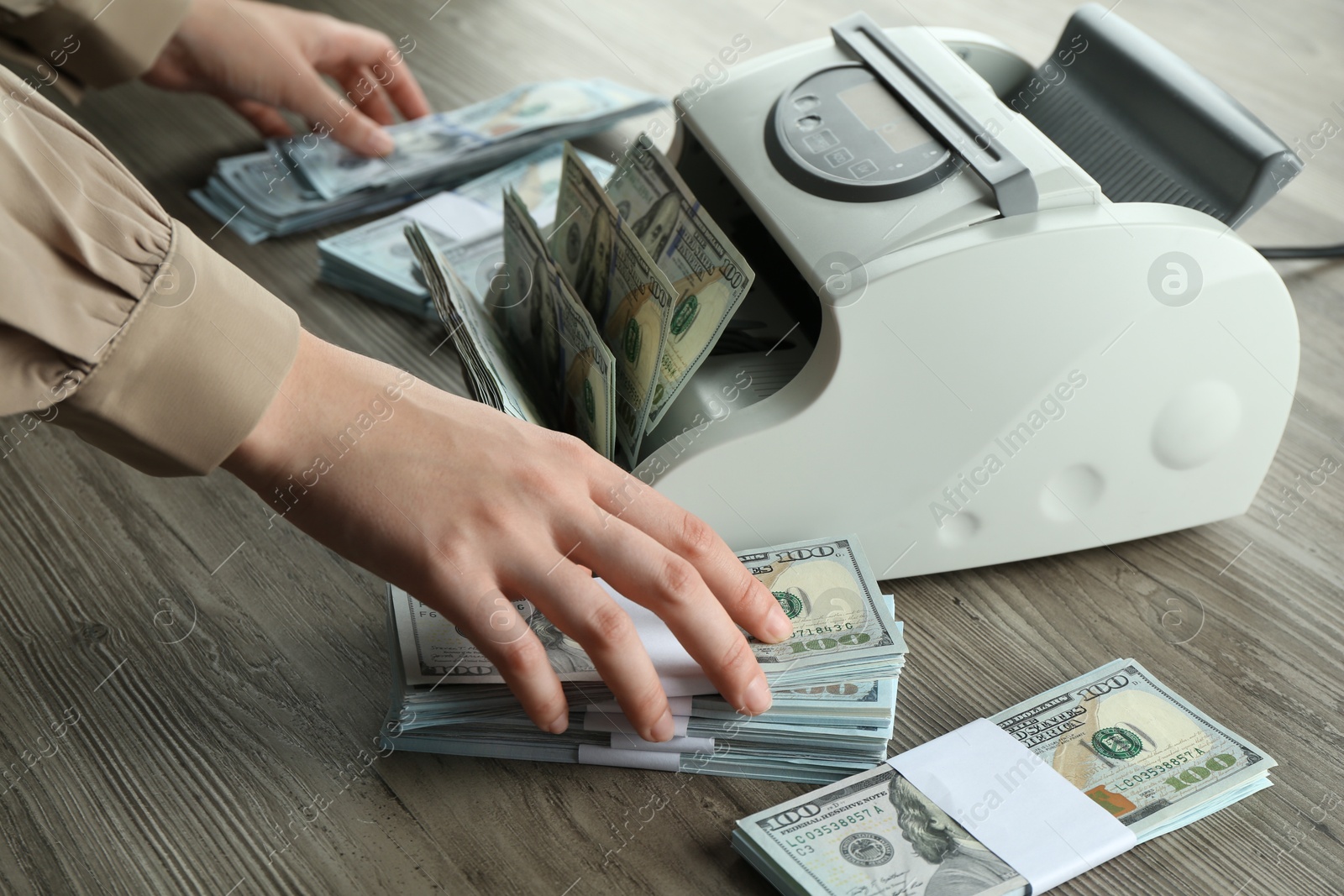 Photo of Woman using money counter machine at wooden table, closeup