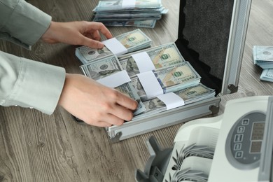 Photo of Woman counting dollar banknotes at wooden table, closeup