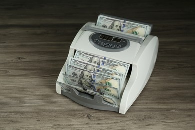 Photo of Money counter machine with dollar banknotes on wooden table