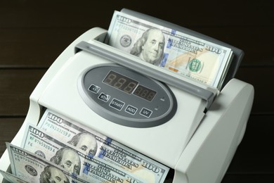 Money counter machine with dollar banknotes on wooden table, closeup