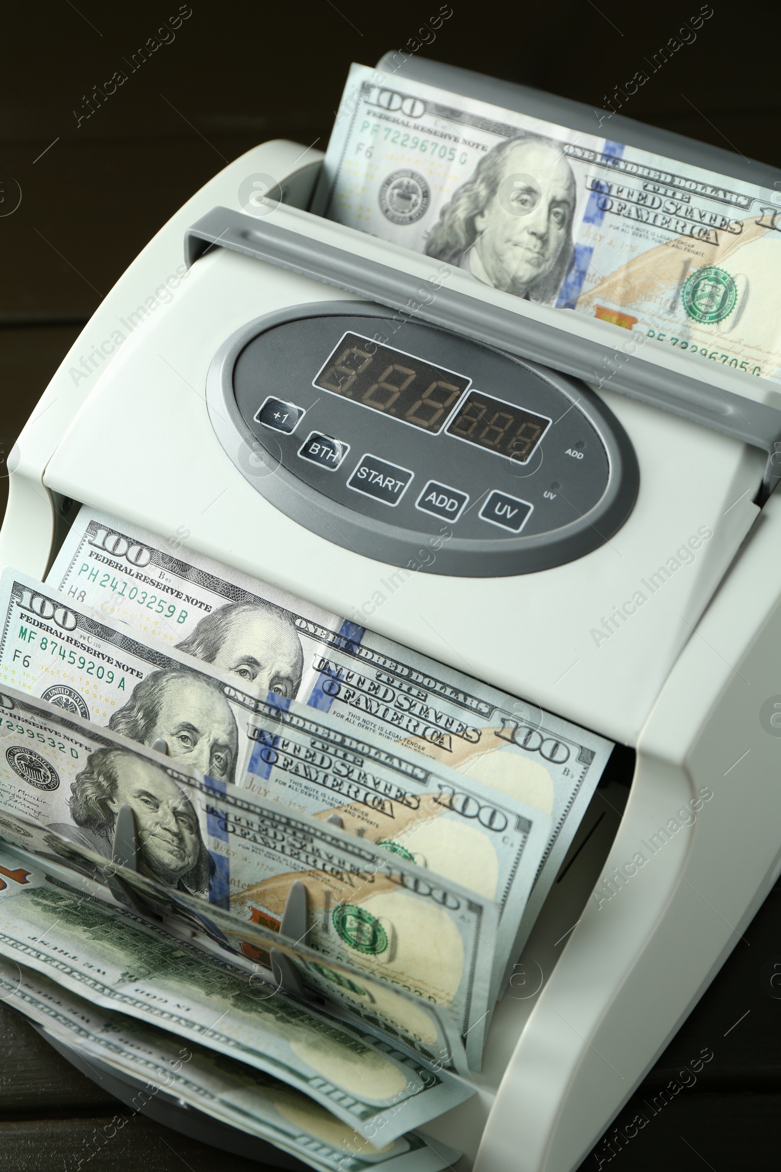 Photo of Money counter machine with dollar banknotes on table, closeup