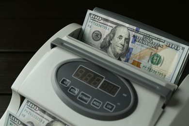 Photo of Money counter machine with dollar banknotes on table, closeup