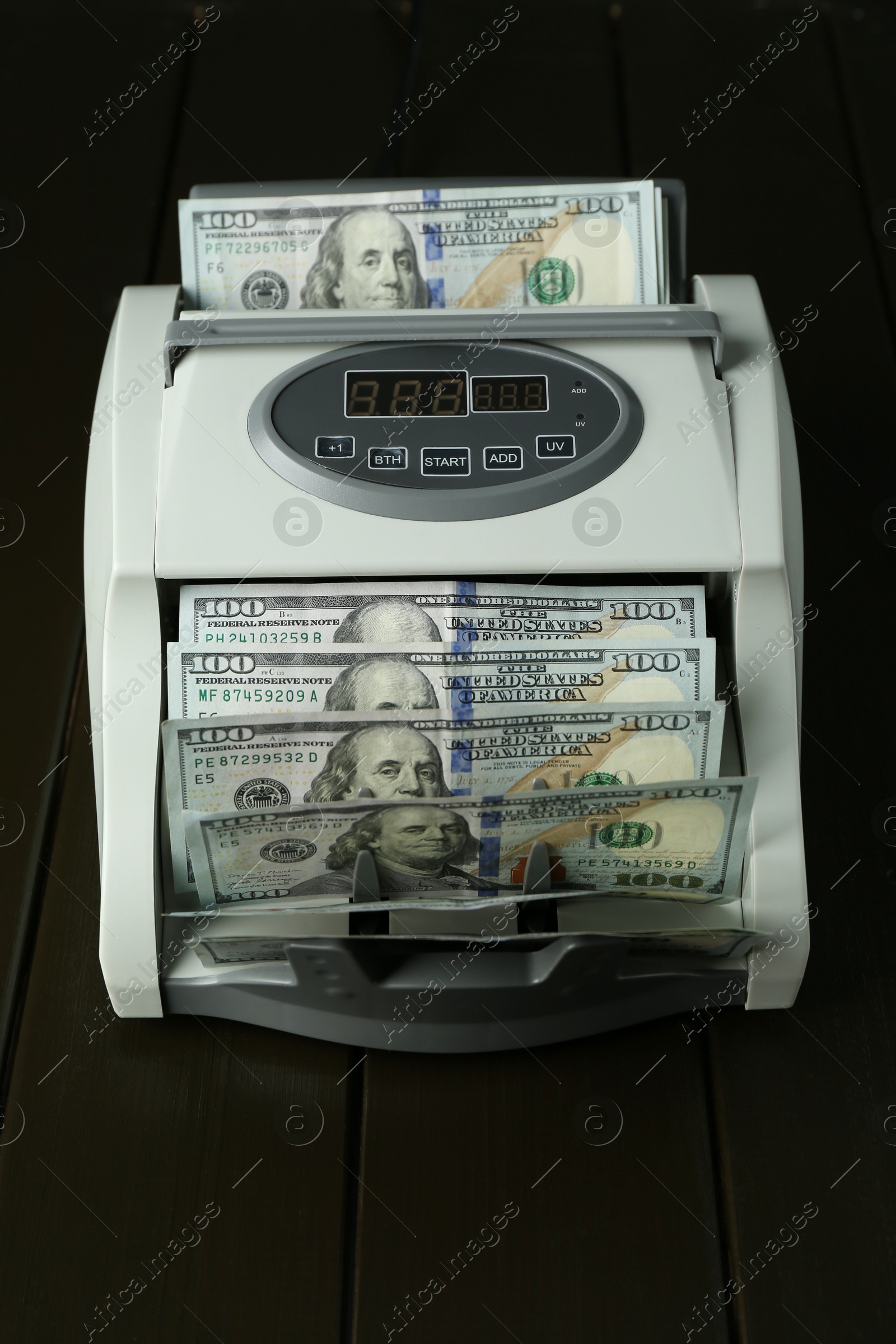 Photo of Money counter machine with dollar banknotes on wooden table