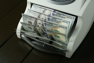 Money counter machine with dollar banknotes on wooden table