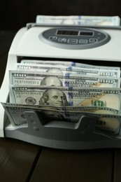 Photo of Money counter machine with dollar banknotes on wooden table