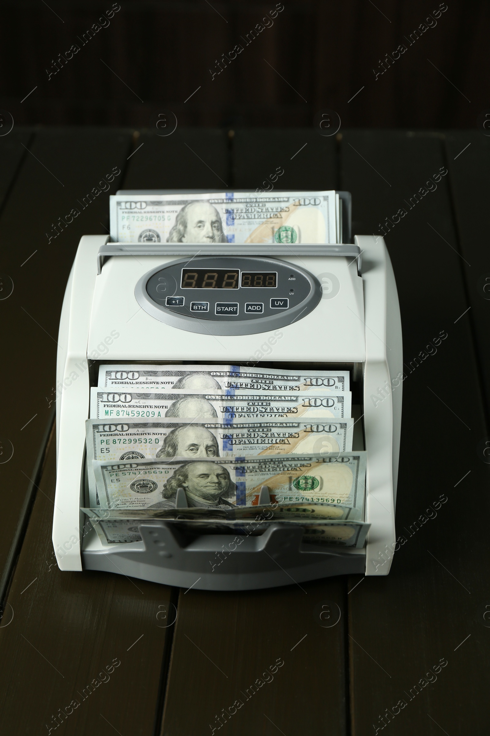 Photo of Money counter machine with dollar banknotes on wooden table