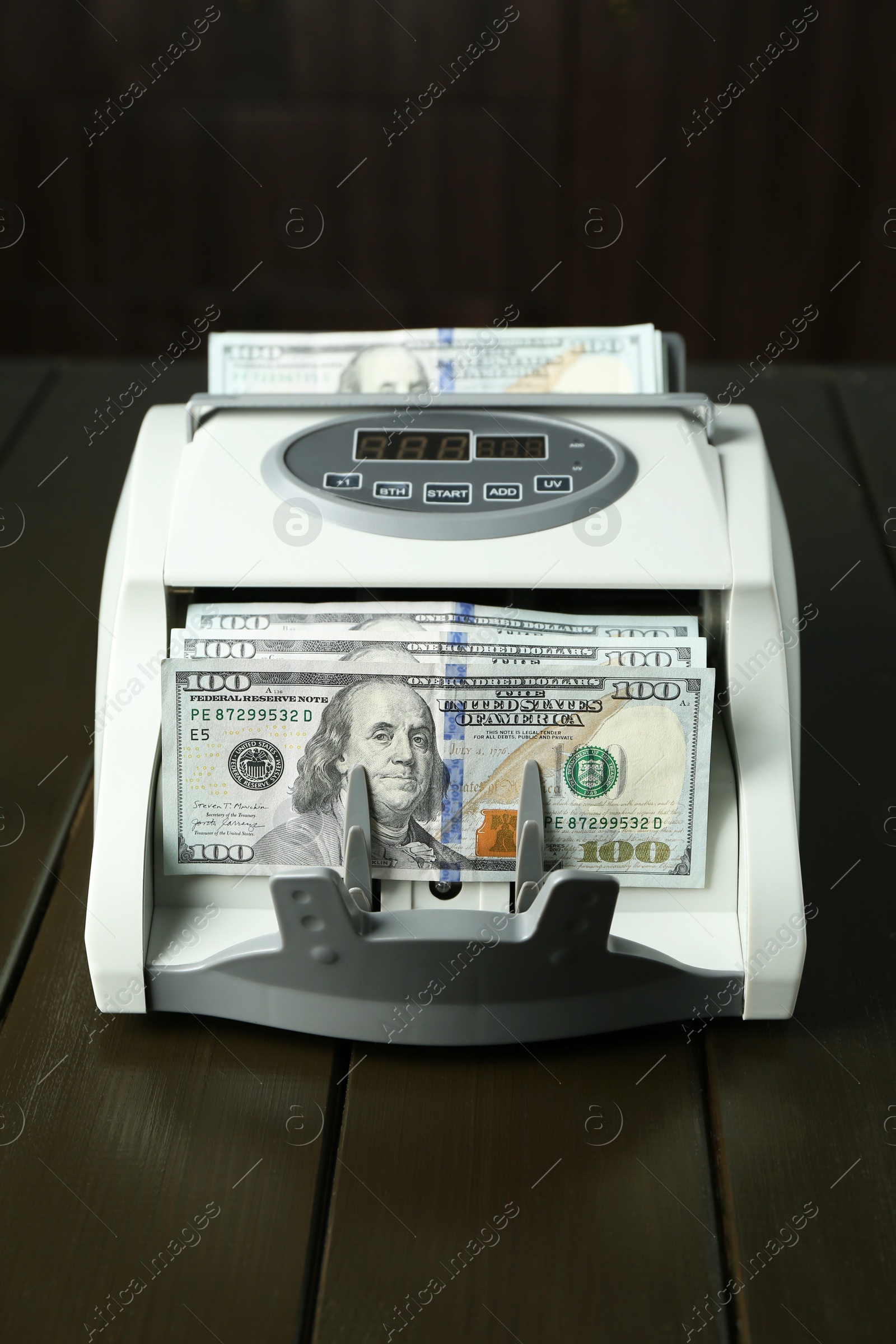 Photo of Money counter machine with dollar banknotes on wooden table