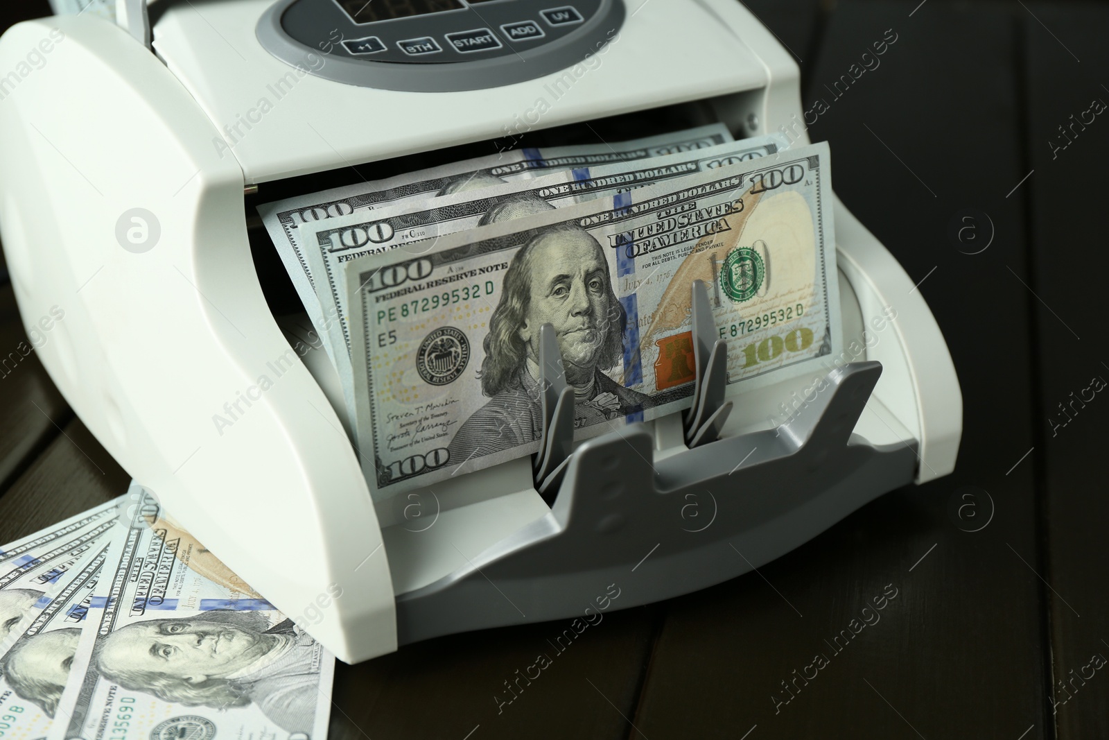 Photo of Money counter machine with dollar banknotes on wooden table