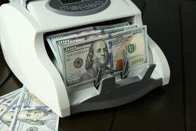 Photo of Money counter machine with dollar banknotes on wooden table