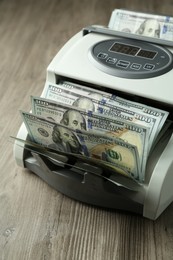 Photo of Money counter machine with dollar banknotes on wooden table