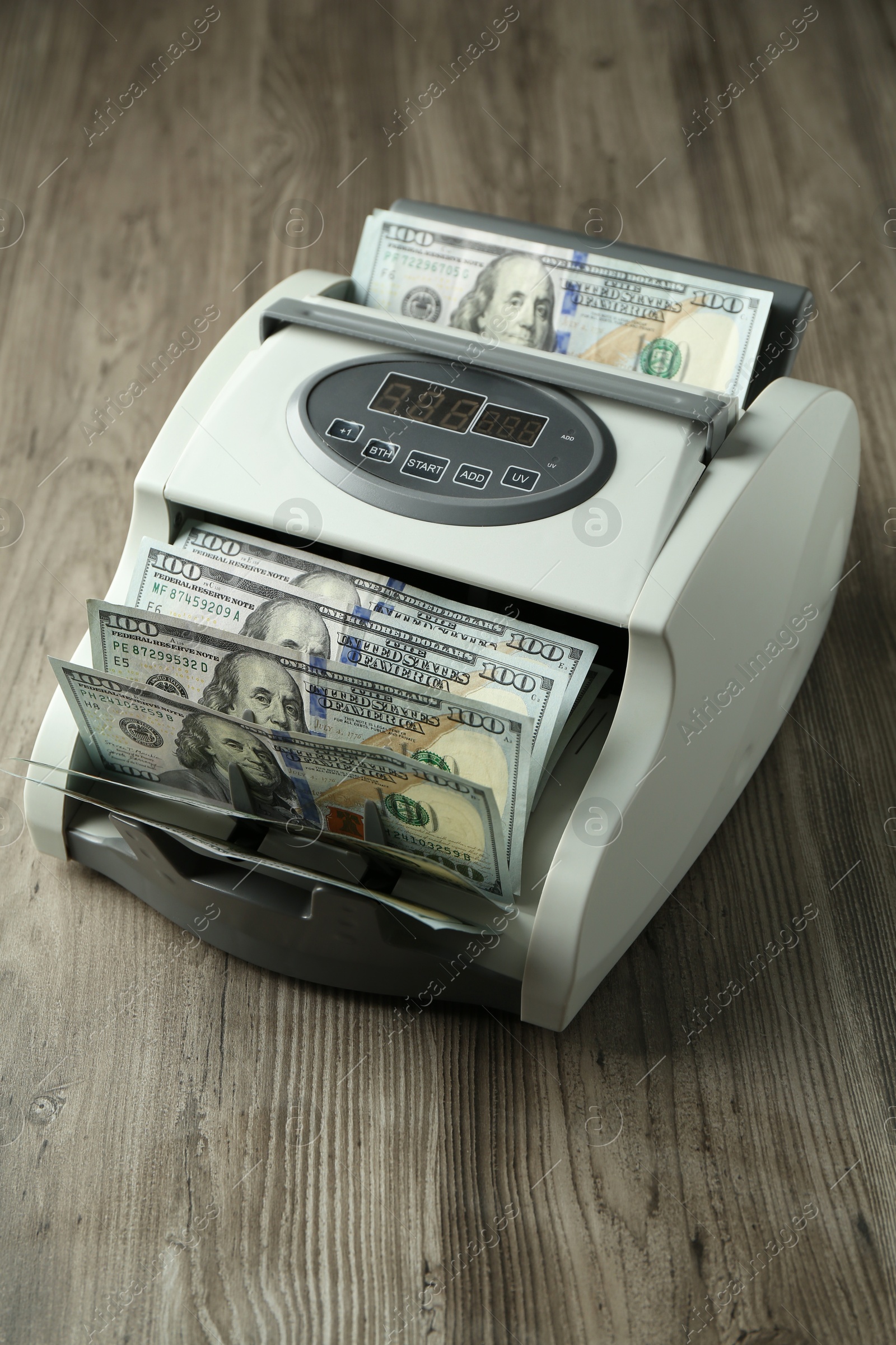 Photo of Money counter machine with dollar banknotes on wooden table