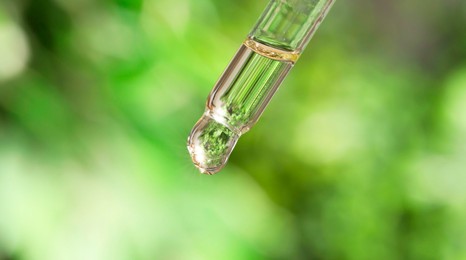 Photo of Essential oil dripping from pipette against blurred green background, closeup. Banner design